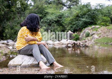 Ragazza isolata seduta da sola su Stone al Calm Lake Shore al mattino Foto Stock