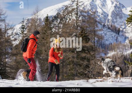 Una coppia gioca a gettare la neve al proprio cane in una giornata all'aperto tra le montagne innevate Foto Stock