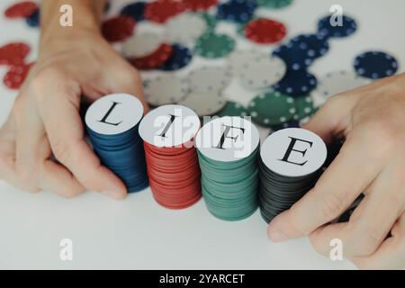 Mani maschili che vanno all-in con una pila di chip da poker colorate con Word LIFE al casinò. Dipendenza dal gioco d'azzardo. Foto Stock