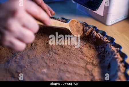Un primo piano di sbriciolate di biscotti graham al cioccolato in una teglia con un cucchiaio di legno, creando la base per un dessert. Uno sguardo dettagliato Foto Stock