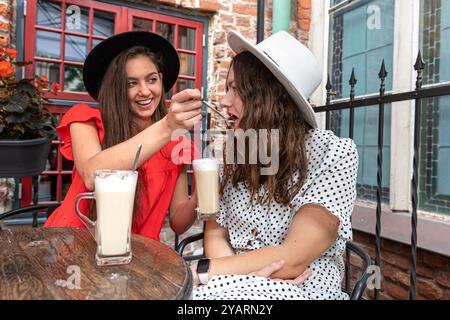 due belle e allegre giovani donne che parlano e ridono in un bar all'aperto, divertendosi insieme Foto Stock