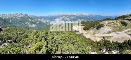 Una fotografia cattura un paesaggio montano soleggiato mozzafiato in una limpida giornata estiva, con lussureggianti colline verdi e vette torreggianti. Foto Stock