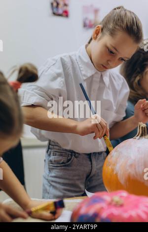 Bambini e adulti dipingono le zucche per Halloween, divertendosi e divertendosi insieme. Foto di alta qualità Foto Stock