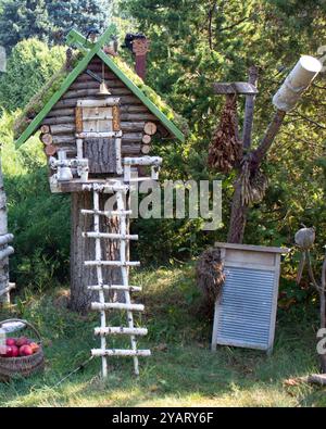 Casa da favola fatta di tronchi di legno con una scala fatta di tronchi di betulla. Accanto alla casa ci sono un lavabo, una scopa e un cestino con mele. T Foto Stock