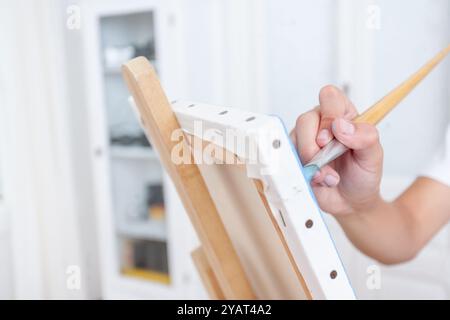 Una persona sta dipingendo un'immagine su una tela con un pennello. Il dipinto è in corso e la persona è concentrata sul suo lavoro Foto Stock