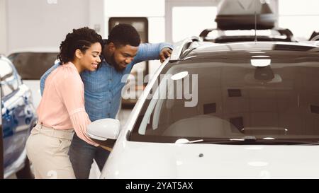 Coppia che sceglie l'auto insieme che si trova vicino al veicolo in showroom, Panorama Foto Stock