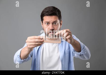 Uomo emotivo che prende i capelli persi dal pettine su sfondo grigio. Problema di alopecia Foto Stock