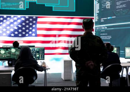 Funzionario dell'esercito AMERICANO che lavora per garantire la protezione dei server e i segreti di stato, proteggendo importanti dati di guerra ibrida nell'ufficio delle agenzie high-tech. Un soldato militare supervisiona l'attività di hacking. Foto Stock