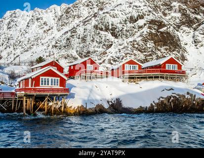 Un villaggio i Lofoten con tradizionali cabine di pescatori in legno rosso su palafitte in acqua, chiamate rorbu, sulle isole Lofoten in inverno. Scandinavo innevato Foto Stock