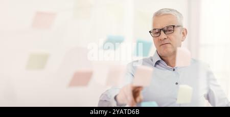 Responsabile anziani che mette le note adesive sulla finestra Foto Stock