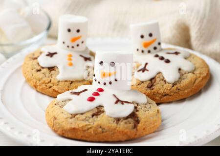 Deliziosi biscotti con pupazzi di neve fatti di marshmallow su tavola bianca, primo piano Foto Stock