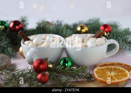 Delizioso cacao con marshmallow in tazze e rami di abete con palle di Natale su tavola bianca Foto Stock