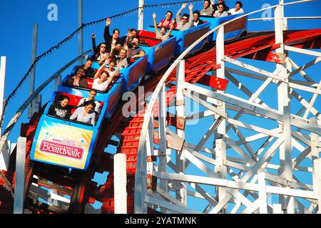 Gli amanti del brivido urlano e alzano le mani mentre scendono sulle storiche montagne russe Giant Dipper in legno a Santa Cruz, California Foto Stock