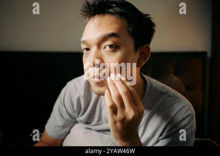 Un uomo che esamina i capelli del viso toccando il mento, apparendo riflessivo e concentrato Foto Stock