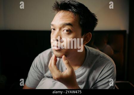 Un uomo che esamina i capelli del viso toccando il mento, apparendo riflessivo e concentrato Foto Stock