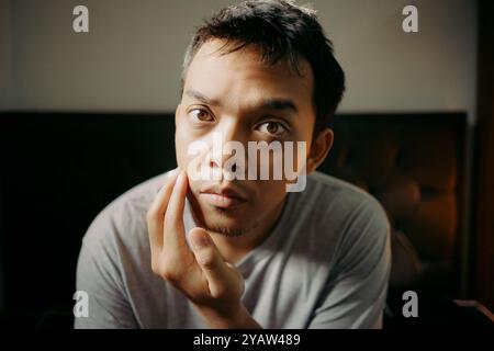 Un uomo che esamina i capelli del viso toccando il mento, apparendo riflessivo e concentrato Foto Stock