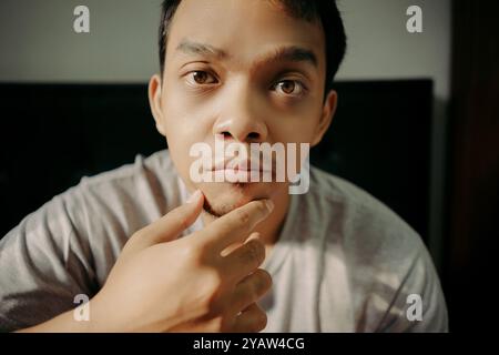 Un uomo che esamina i capelli del viso toccando il mento, apparendo riflessivo e concentrato Foto Stock