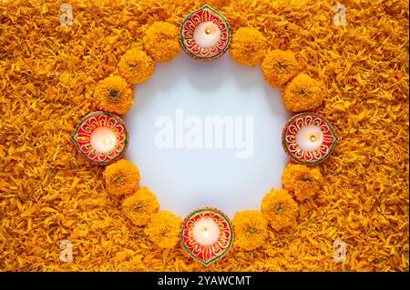 Rangoli decorativi di fiori di calendula e petali di colore arancione con lampada diya in argilla per il festival Diwali su sfondo bianco. Foto Stock