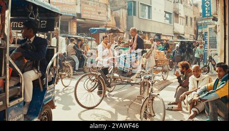 Varanasi, India. La gente cammina lungo la strada trafficata. I conducenti di Mans Rickshaw riposano e bevono caffè. Traffico su Street Motion. Motociclette, in movimento per strada Foto Stock