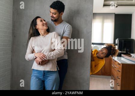 La bella coppia multietnica passa del tempo insieme, abbracciando e sorridendo con il bambino sullo sfondo Foto Stock