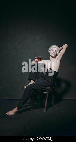 Uomo che posa drammaticamente con un drink, con una rivisitazione giocosa della decadenza aristocratica, che fonde storia con stile contemporaneo. Foto Stock