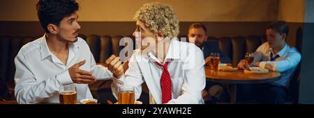 Banner. Due uomini si impegnano in una vivace discussione al tavolo del bar mentre i loro colleghi in sottofondo si godono bevande e cibo. Foto Stock