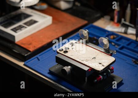 Smartphone con vetro rotto sul tavolo di riparazione durante l'assistenza tecnica in un'officina affollata Foto Stock