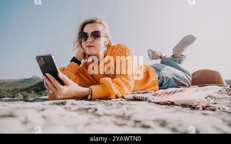 Donna in maglione giallo utilizza il telefono su una montagna Foto Stock