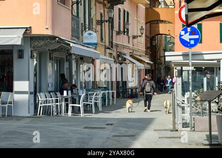 Una ragazza da dietro porta due cani al guinzaglio nella strada pedonale principale ("budello") in primavera, Alassio, Savona, Liguria, Italia Foto Stock