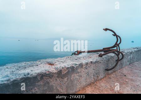 Un'ancora arrugginita si trova su un muro di cemento vicino all'oceano Foto Stock