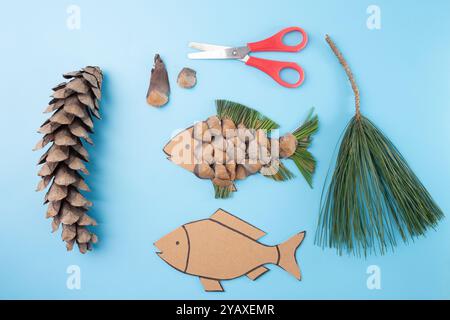 Fai da te, pesca artigianale con scaglie di pino, aghi di pino e cartone con forbici rosse su sfondo beige. Composizione piatta per la lavorazione, riciclo Foto Stock