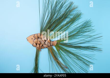 Forma di pesce composta da coni di pino e aghi di pino su sfondo blu. Composizione piatta. Concetto artistico ispirato alla natura. Design per poster e biglietti d'auguri Foto Stock