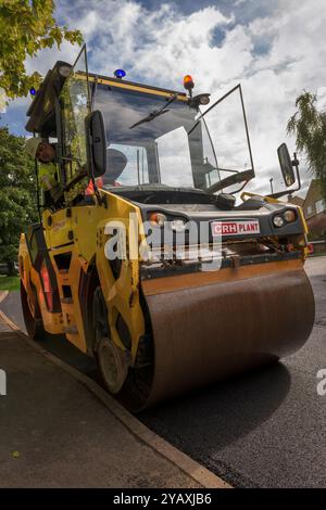 Un team di operai che gestiscono macchinari pesanti per ripavimentare una strada residenziale nel Wiltshire. Foto Stock