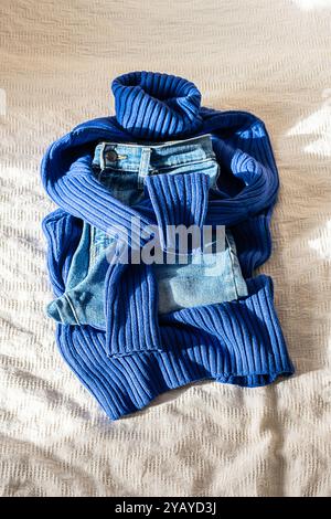 Maglione caldo alla moda con colletti alti e jeans blu sul letto. Vestito autunnale. Foto Stock