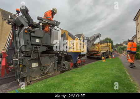 Un team di operai che gestiscono macchinari pesanti per ripavimentare una strada residenziale nel Wiltshire. Foto Stock