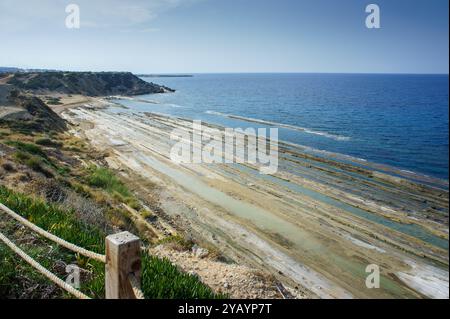 Una tranquilla distesa lungo la costa mostra formazioni rocciose a strati sotto il mare calmo, scintillanti sotto un ampio cielo al tramonto. Foto Stock