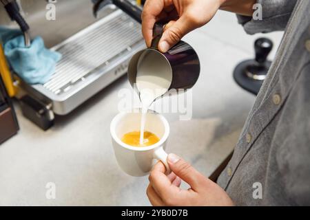 Il barista versa sapientemente il latte montato nell'espresso per creare un Cappuccino perfetto Foto Stock