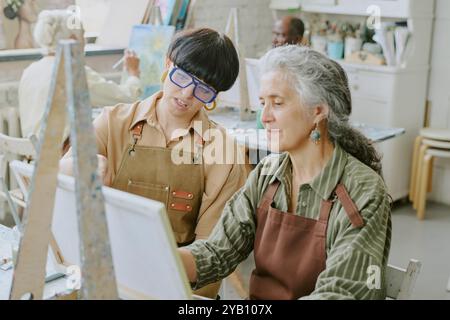 Ripresa ad alto angolo di una giovane insegnante di disegno professionista che dà consigli mentre una studentessa anziana lo ascolta attentamente Foto Stock