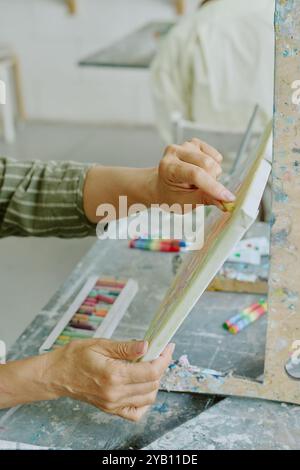 Scatto ad angolo alto di mani femminili irriconoscibili che tengono in mano tela bianca e dipingono schizzi con gesso pastello Foto Stock