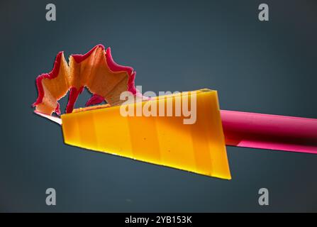 La matita rosa viene affilata da un affilatore arancione, lasciando i trucioli sulla parte superiore. Foto Stock