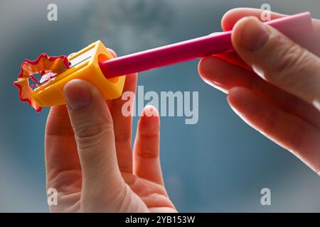 La persona sta affilando una matita rosa con un piccolo affilatore giallo. Foto Stock