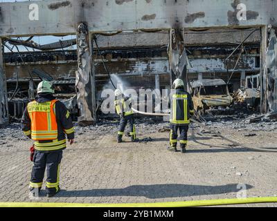 Stadtallendorf, Germania. 16 ottobre 2024. I vigili del fuoco sono impegnati a spegnere il fuoco. Il nuovo deposito di attrezzature del dipartimento dei vigili del fuoco volontario di Stadtallendorf è completamente bruciato con veicoli e attrezzature, causando milioni di danni. Crediti: Andreas Arnold/dpa/Alamy Live News Foto Stock