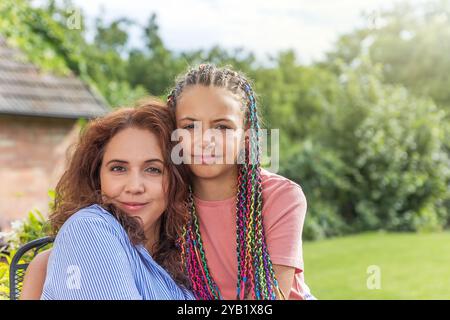 Ritratto di madre e figlia dai capelli lunghi che guardano la macchina fotografica che posa in giardino. Orizzontalmente. Foto Stock