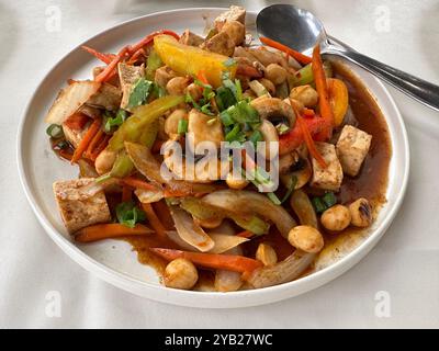 Un piatto fresco di verdure saltate, composto da cipolla, peperone, funghi, sedano, tofu e noci di macadamia in salsa tailandese sono mostrati da vicino. Foto Stock