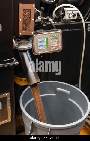 I chicchi di caffè tostati subito dopo la tostatura vengono versati dalla macchina per torrefazione industriale in un contenitore di raccolta, foto ravvicinate con effetto di sfocatura in movimento Foto Stock