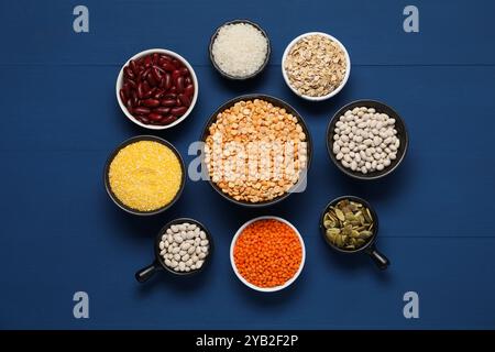 Diversi tipi di cereali, semi e legumi su un tavolo di legno blu, piatto Foto Stock