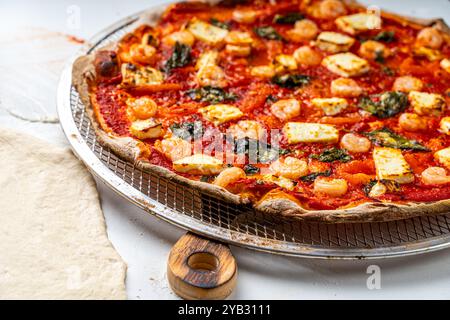 Pizza con frutti di mare, pomodoro e basilico su una griglia, su un tavolo bianco accanto all'impasto arrotolato. Foto di alta qualità Foto Stock