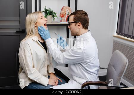 Il medico utilizza la spatola per ispezione per esaminare la gola del paziente. Medico ENT che fa esame di gola di una donna. La paziente aprì il check-up bocca-gola. Foto Stock