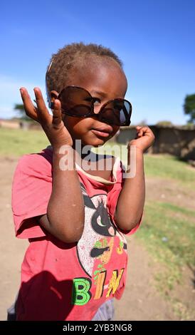 RISERVA NAZIONALE MAASAI MARA, KENYA, AFRICA - 11 NOVEMBRE 2022: I bambini simpatici Maasai cercano occhiali da sole turistici. Villaggio di Maasai in Kenya, Africa Foto Stock