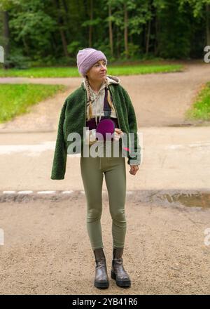 Giovane donna con il braccio rotto che cammina lentamente all'aperto. La paziente indossa un'imbracatura per sostenere il braccio. Incidente. Assicurazione sulla vita Foto Stock